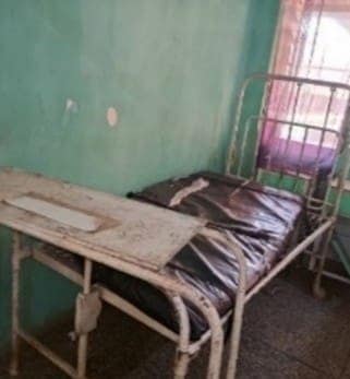 An old, worn hospital bed in a rundown room with peeling green walls.